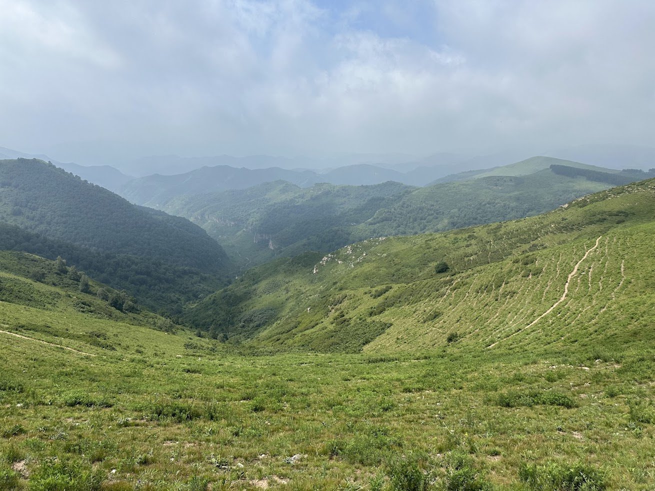 Green valley and hazy mountain ridges under a cloudy sky